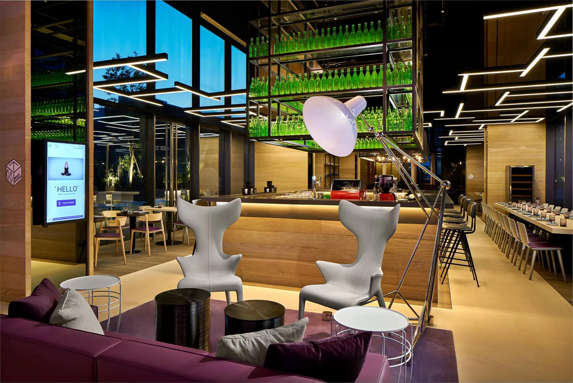 Evening lobby lounge with wing chairs, purple sofas and bottle installation — YOTEL Singapore hospitality photography