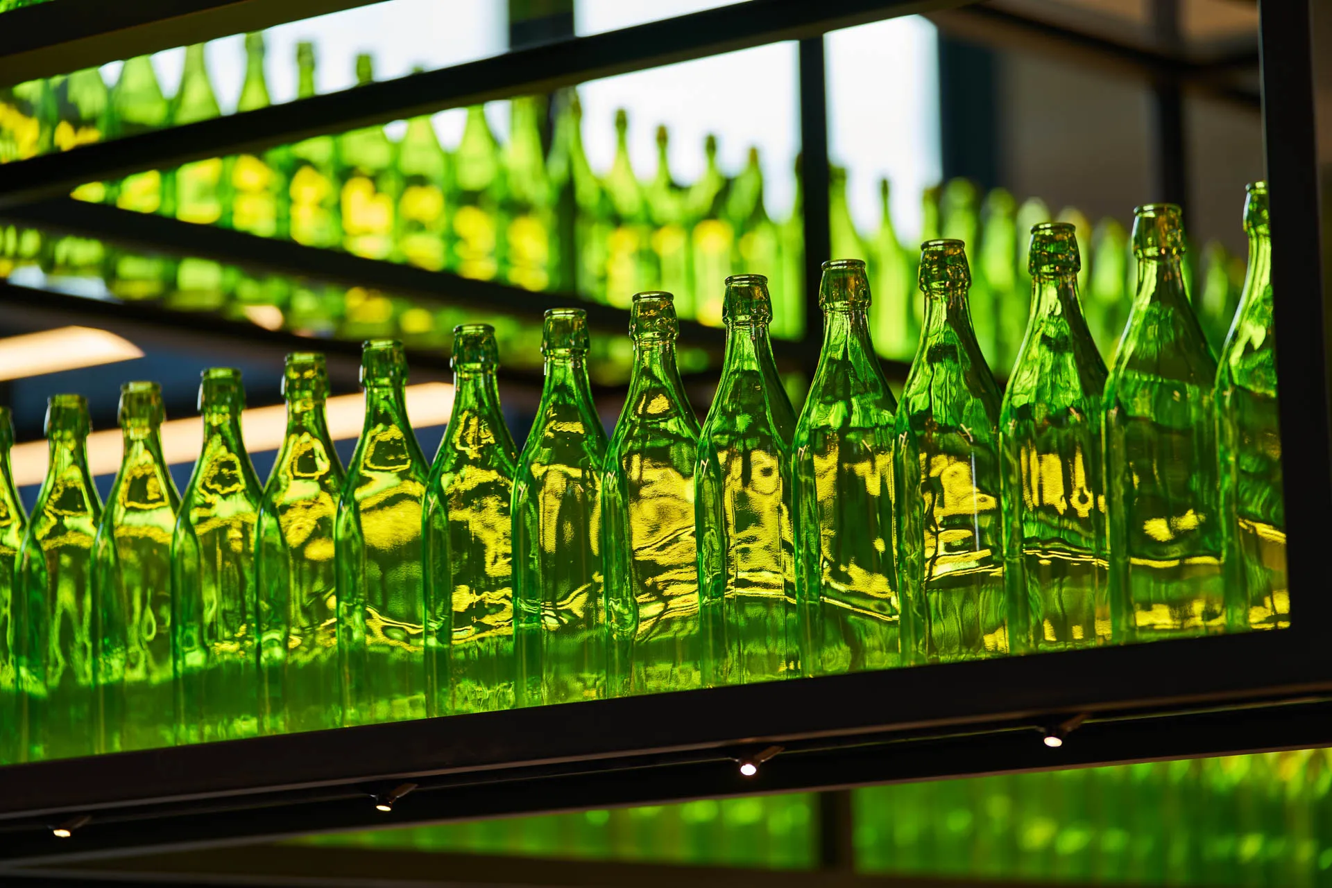 Backlit green glass bottles on black metal bar shelving — YOTEL Singapore restaurant photography