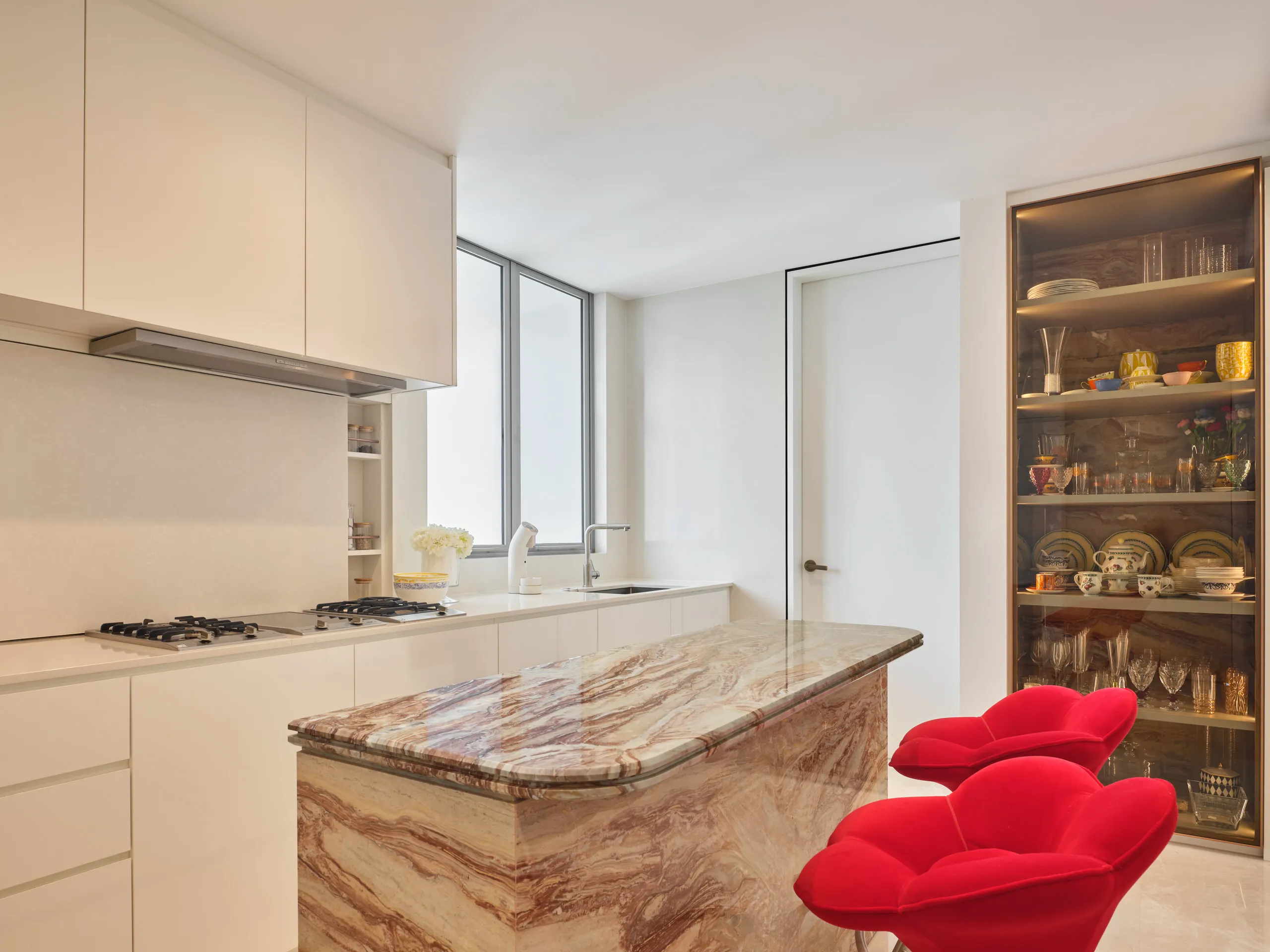 Interior design photography of a modern kitchen with marble countertops, sleek cabinetry, and a striking red accent chair.