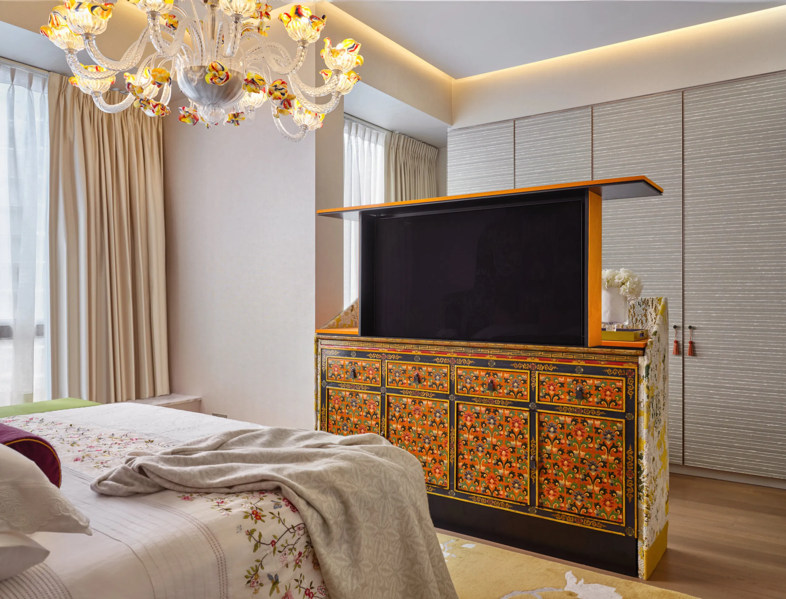Interior design photography of a bedroom featuring an ornate TV console at the foot of the bed in a raised position, blending functionality with luxury design.