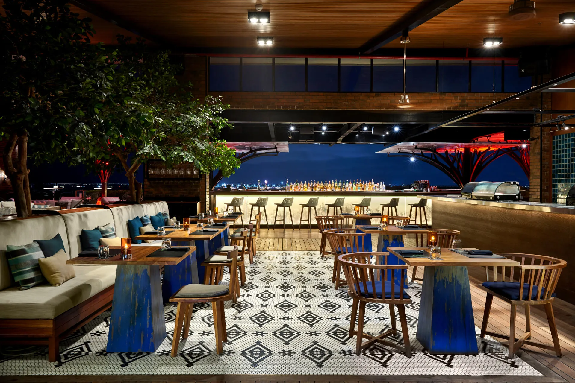 Dining room with mosaic floor, trestle tables and indoor tree at night — Above Eleven Bali interior photography
