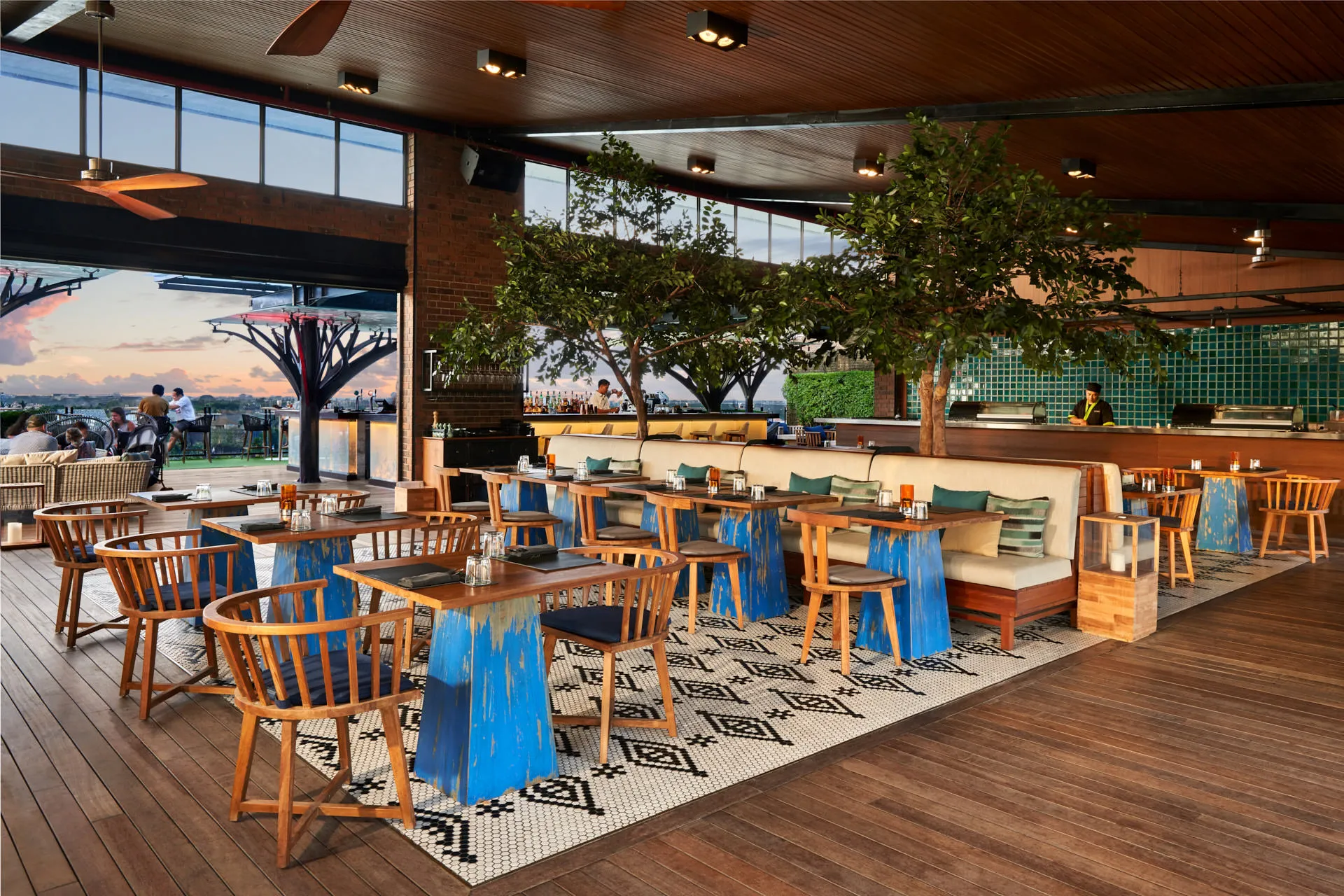 Restaurant at dusk with open kitchen, indoor trees and sunset through canopies — Above Eleven Bali interior photography