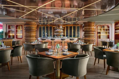 Ce La Vi rooftop restaurant interior with emerald velvet seating, bronze sculptural columns, and geometric mirrored ceiling with golden lighting