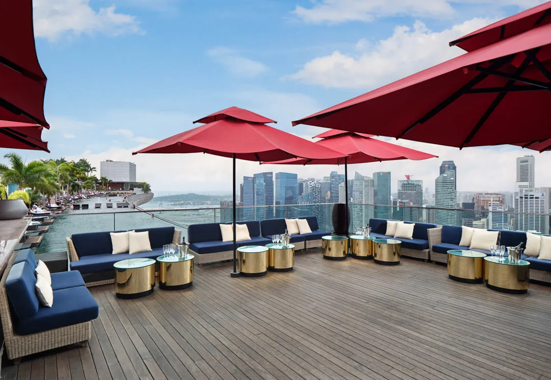 Rooftop lounge with navy sofas, gold tables and Singapore skyline — CÉ LA VI Singapore hospitality photography