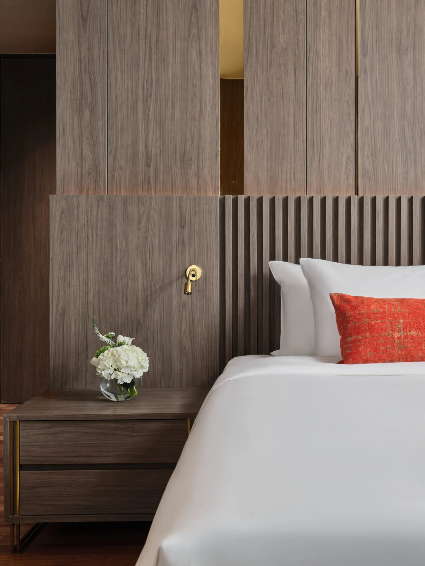 Bedside detail with brass sconce, hydrangeas and walnut slatted headboard — Fraser Suites Sukhumvit hotel photography