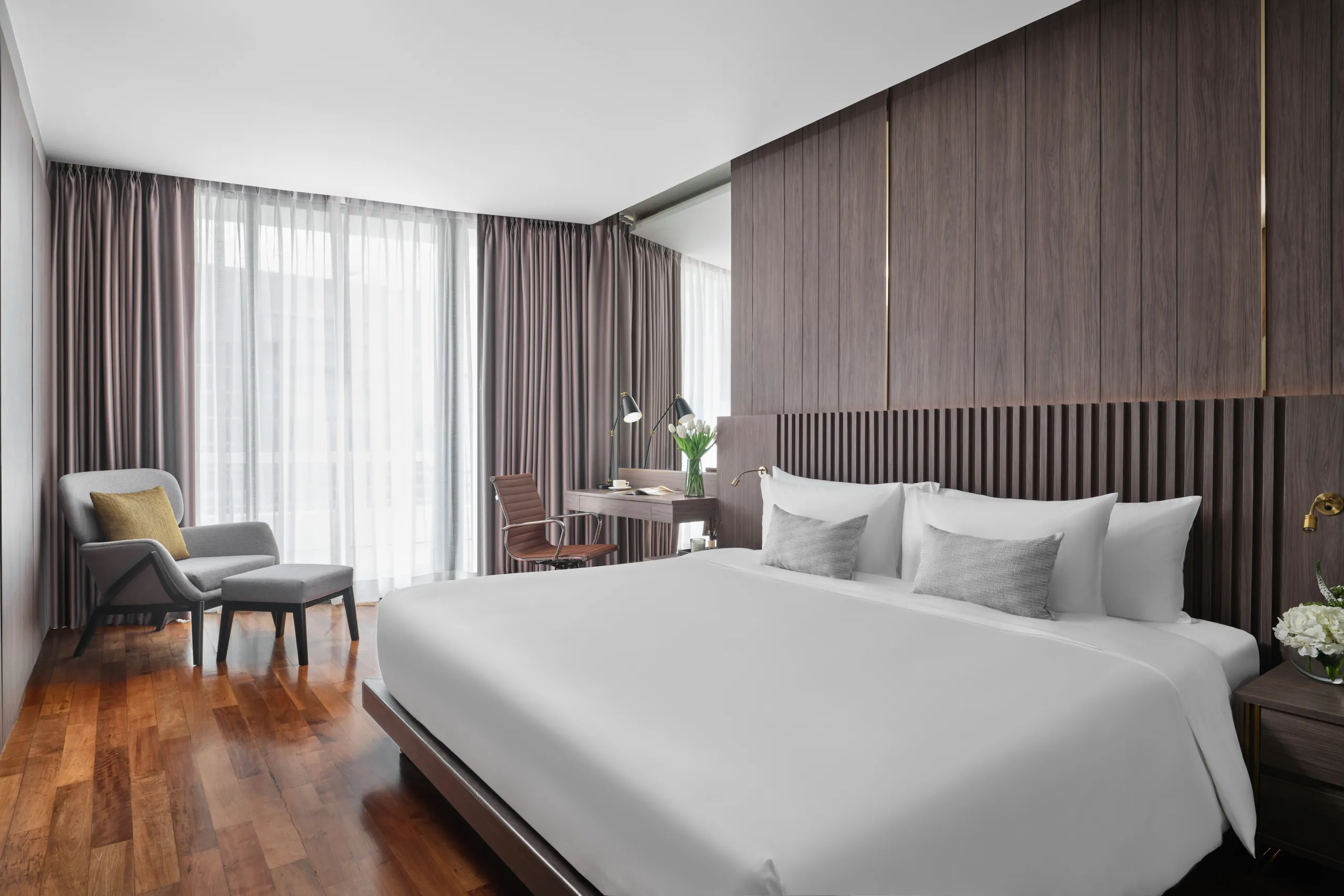 Suite king bedroom with walnut slatted headboard and grey lounge chair — Fraser Suites Sukhumvit hospitality photography