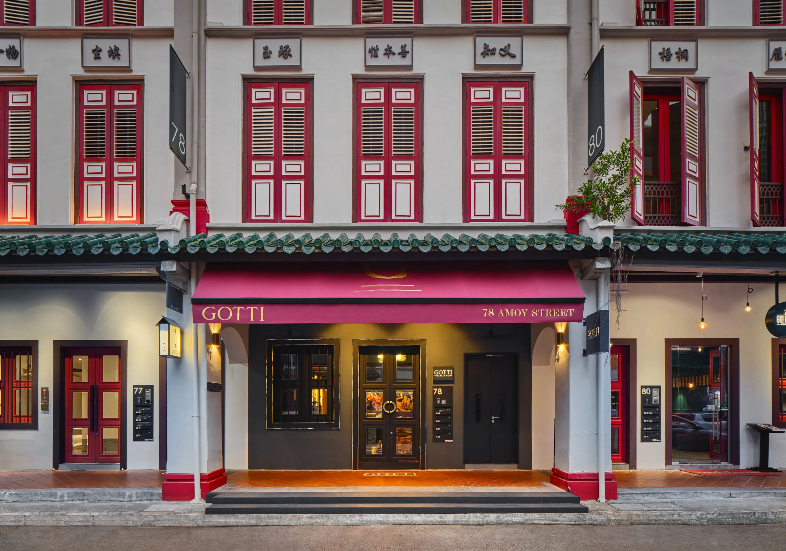 F&B interior design photography of Gotti Singapore, showcasing its historic facade with red windows and a warmly lit entrance at dusk.