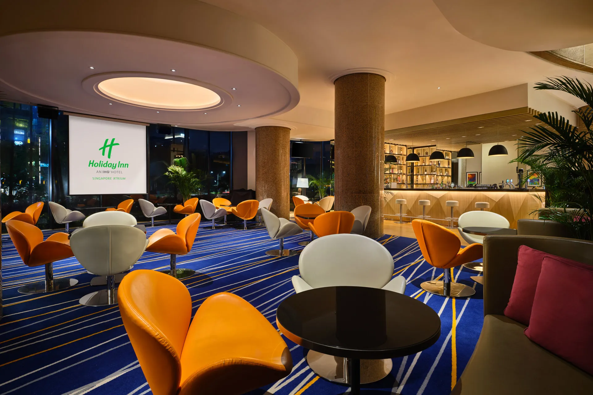 Evening lounge with orange tulip chairs, cocktail tables and warm lighting — Holiday Inn Atrium Singapore hospitality photography