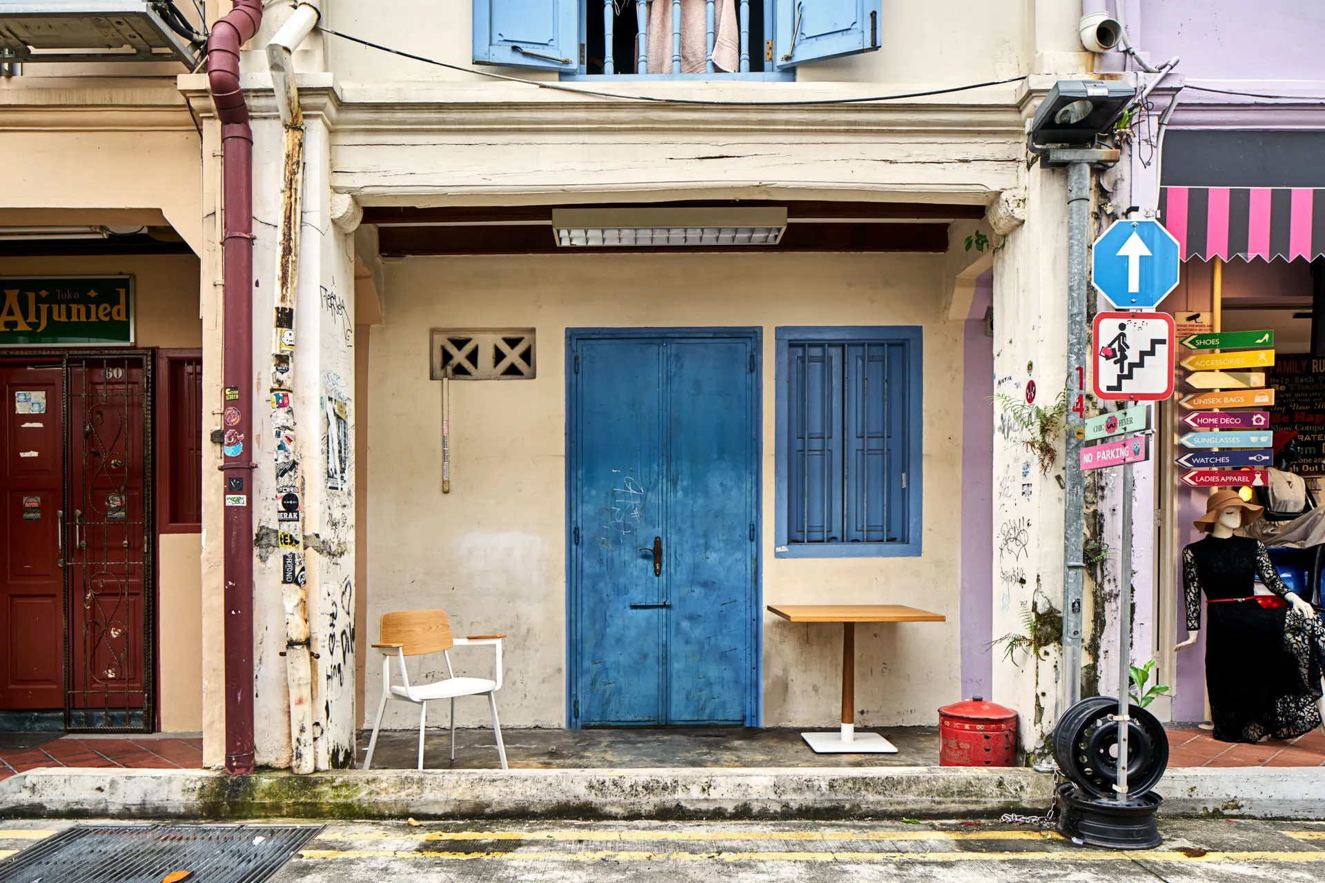 Wooden chair and cafe table beside blue shophouse door and graffiti — Momentum Creations Singapore product photography