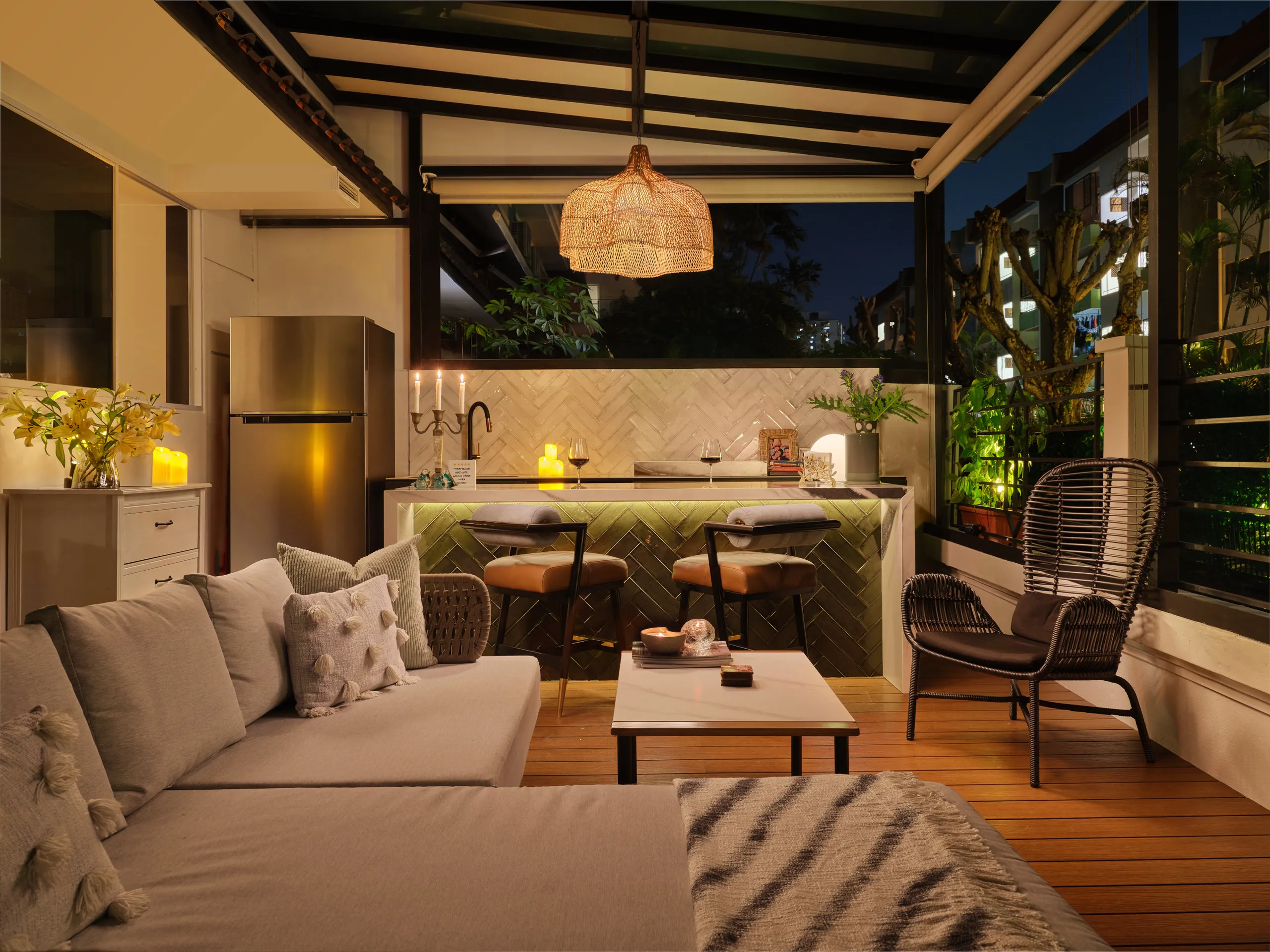 Residential interior design photography of an outdoor bar area in East Coast Singapore, with warm lighting, woven textures, and a cozy seating arrangement featuring Nidhi Jain the designer.