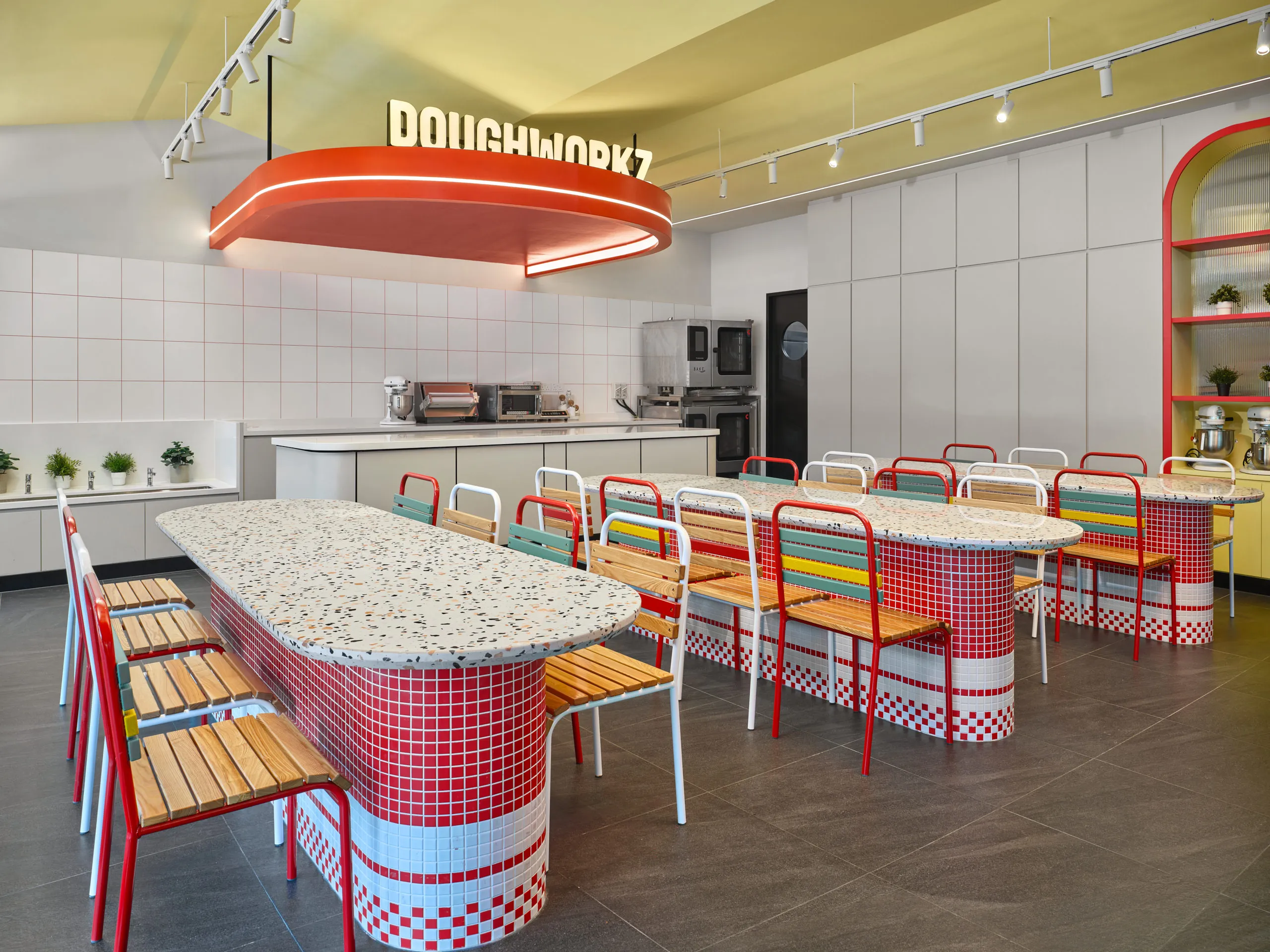 Doughworkz prep kitchen with communal tables and red oval pendant — PastaMania interior design photography