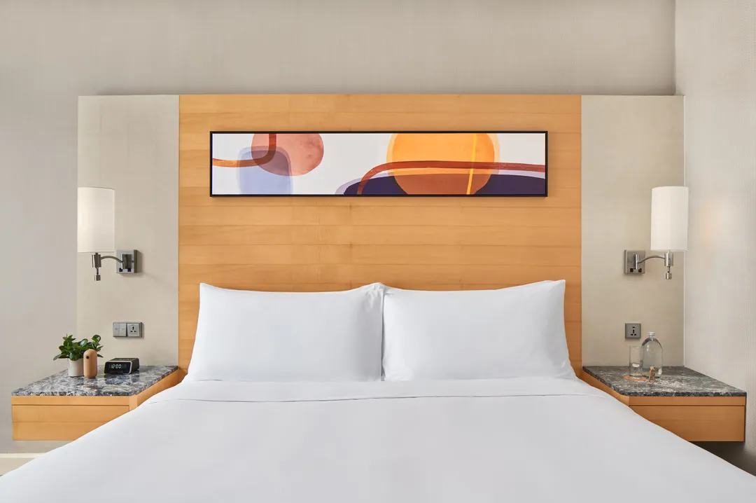 King bed with abstract painting, marble nightstands and chrome sconces — voco Orchard Singapore hotel photography