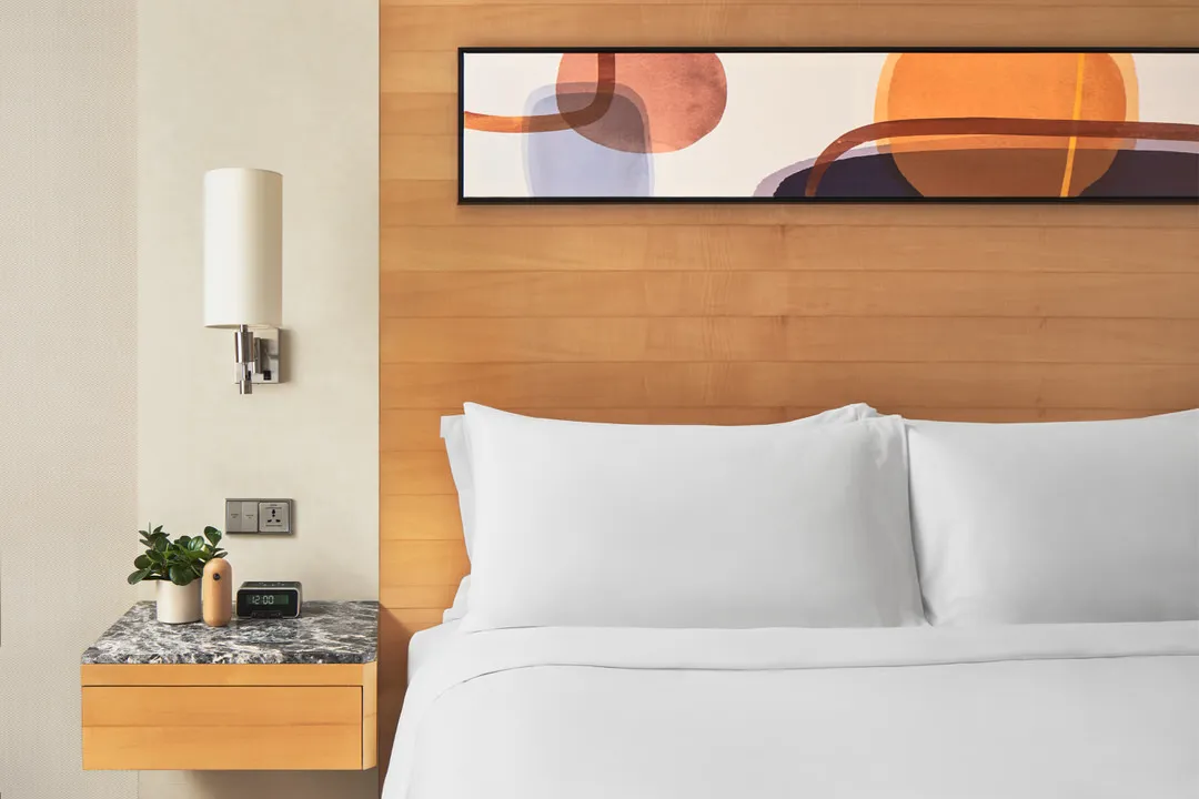 Bedside detail with maple headboard, marble nightstand and chrome sconce — voco Orchard Singapore interior photography