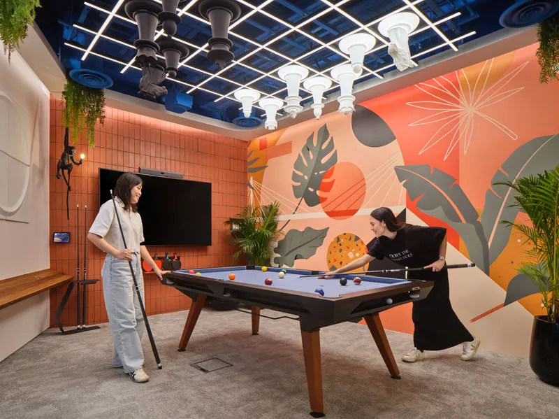 Two employees playing pool in a creative office games room on a convertible conference table, with a unique chess set mounted on the ceiling and a monkey statue in the corner—a prime example of modern workplace photography in Singapore.