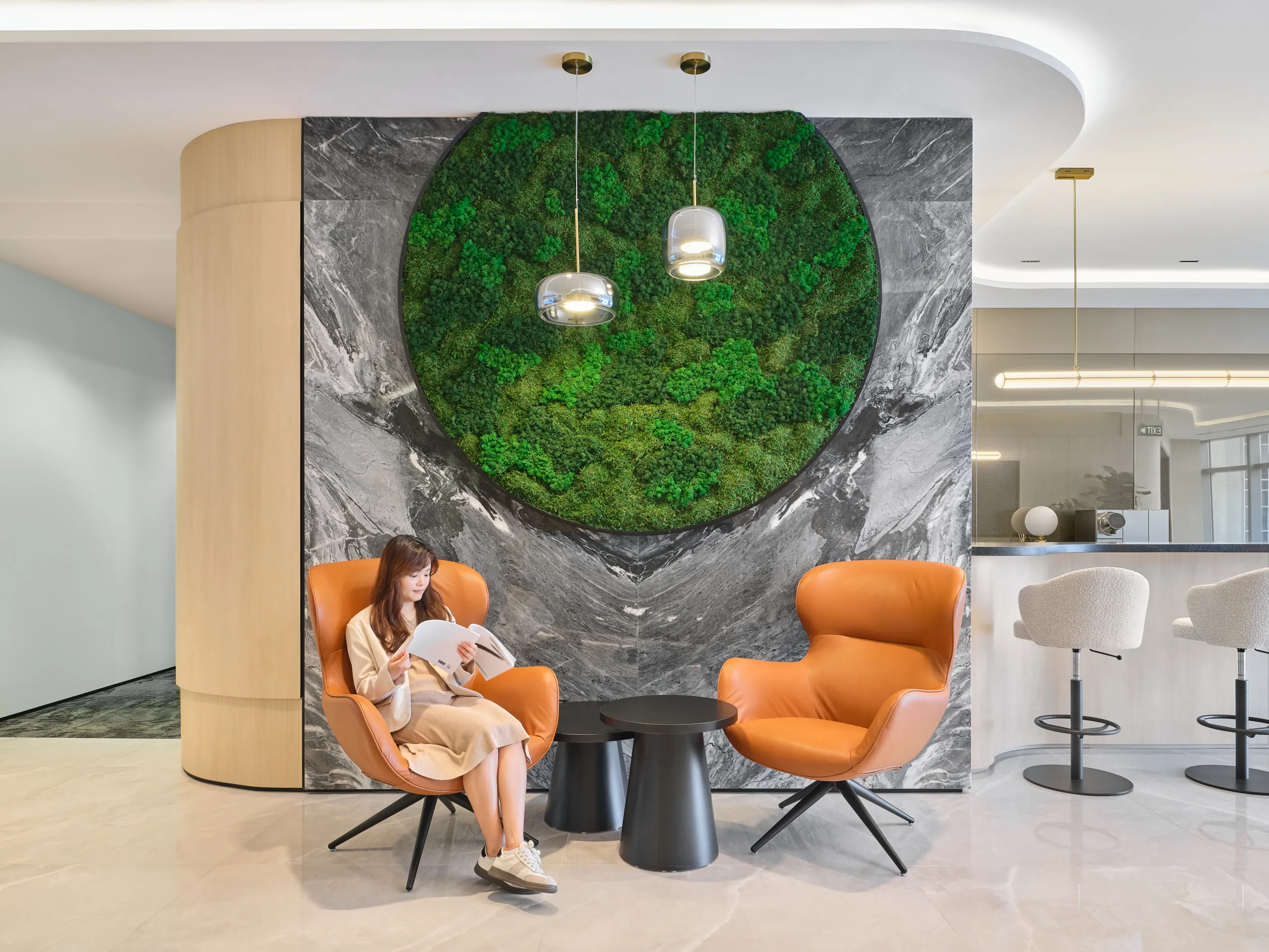 Reception detail with cognac wingback chairs and glass pendants beside moss wall — Singapore office photography